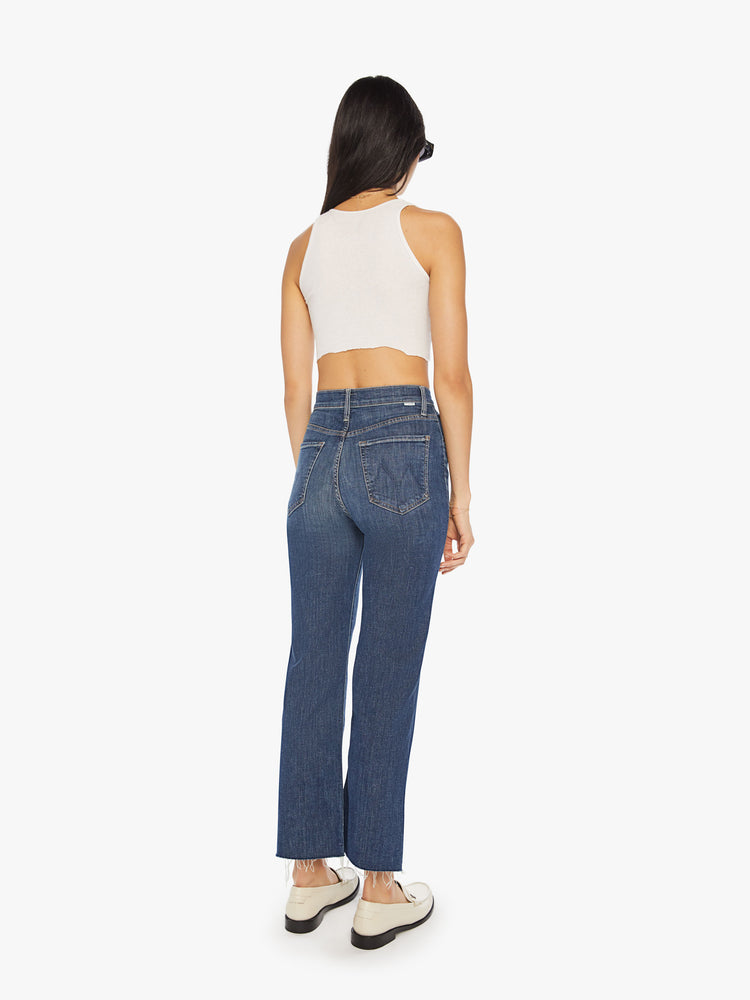 Back view of a womens dark blue denim jean featuring a high rise, a wide straight leg, and ankle length raw hem.