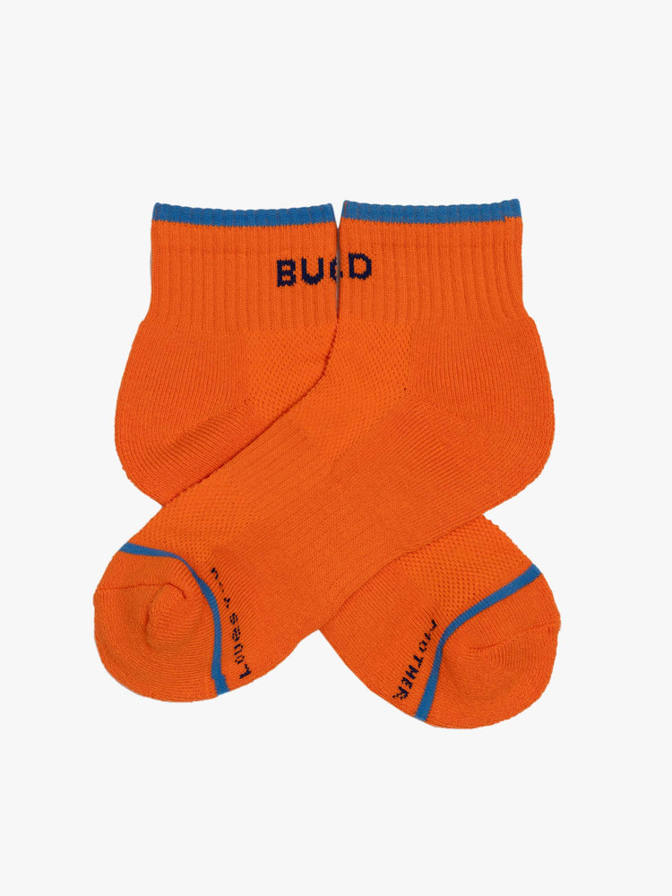 Side flat view of a orange with blue text ankle-length tube socks with a subtle heads up from MOTHER. 