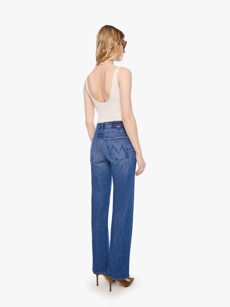 Back view of a petite woman in mid blue high-rise straight leg jean with a zip fly, long 30-inch inseam and a clean hem.