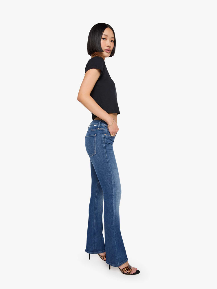 Side view of a woman med blue in a skinny flare with a mid rise, zip fly and a long 30-inch inseam with a clean hem.