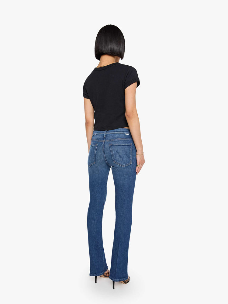 Back view of a woman med blue in a skinny flare with a mid rise, zip fly and a long 30-inch inseam with a clean hem.