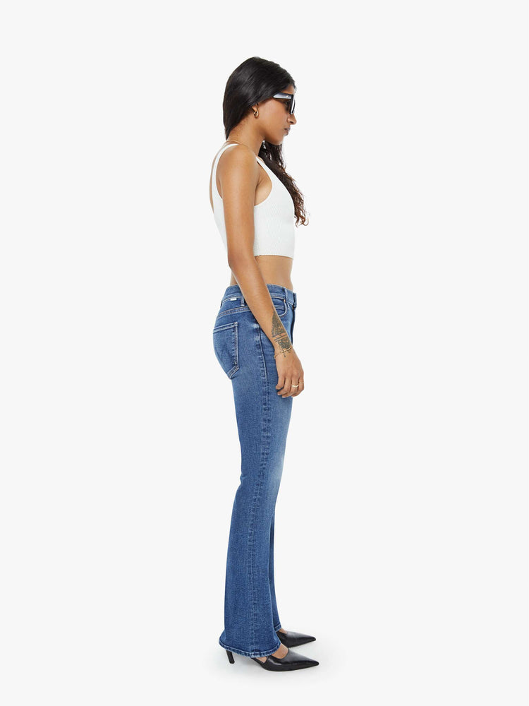 Side view of a petite woman in a med blue  classic skinny flare with a mid rise, zip fly and a long 31-inch inseam with a clean hem. 