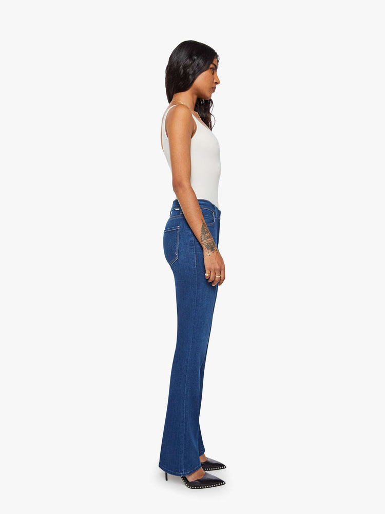 Side view of a petite woman in a dark blue skinny flare with a mid rise, zip fly and a long 30-inch inseam with a clean hem.
