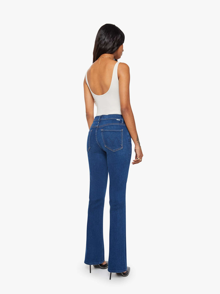 Back view of a petite woman in a dark blue skinny flare with a mid rise, zip fly and a long 30-inch inseam with a clean hem.