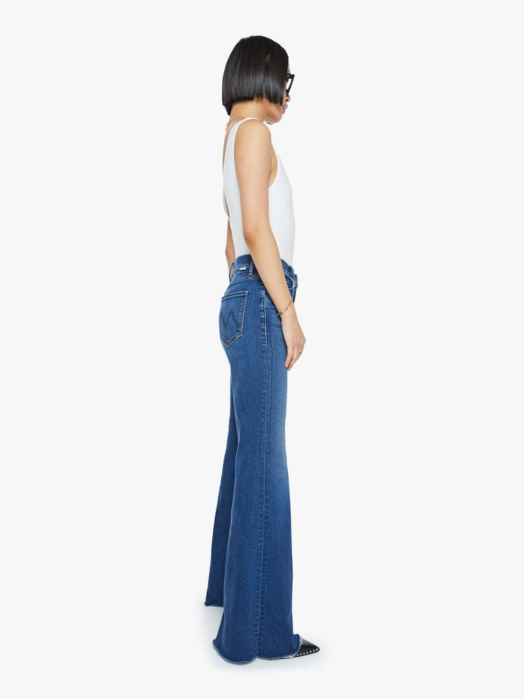 Side view of a mid blue high-rise flare with a long 31-inch inseam and a frayed hem.