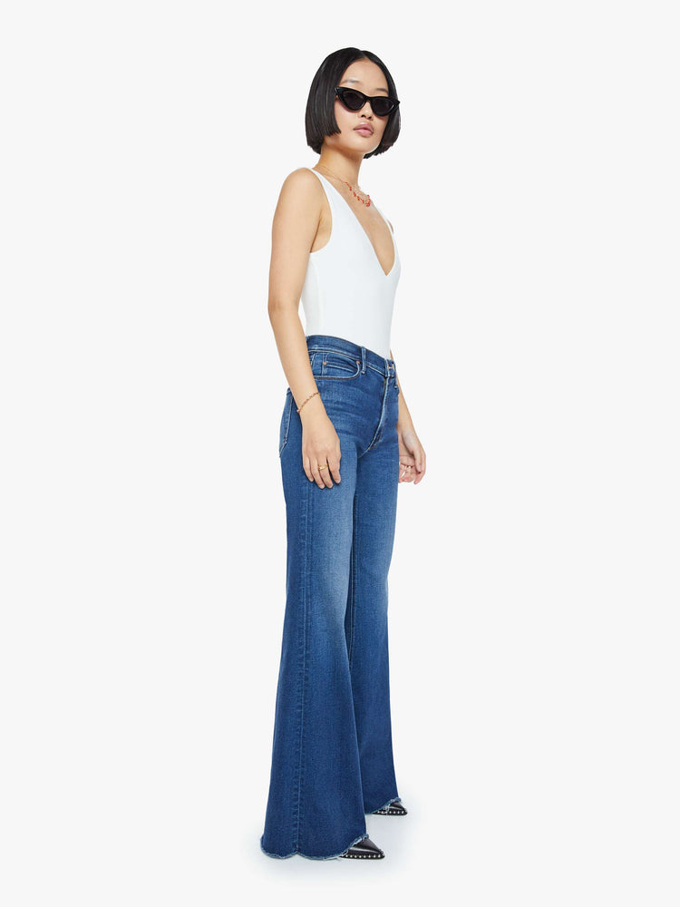 Side angle view of a mid blue high-rise flare with a long 31-inch inseam and a frayed hem.