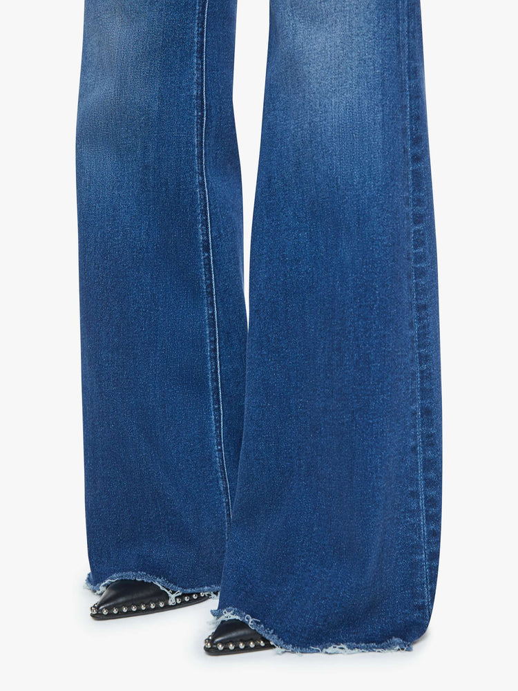 Hem view of a mid blue high-rise flare with a long 31-inch inseam and a frayed hem.