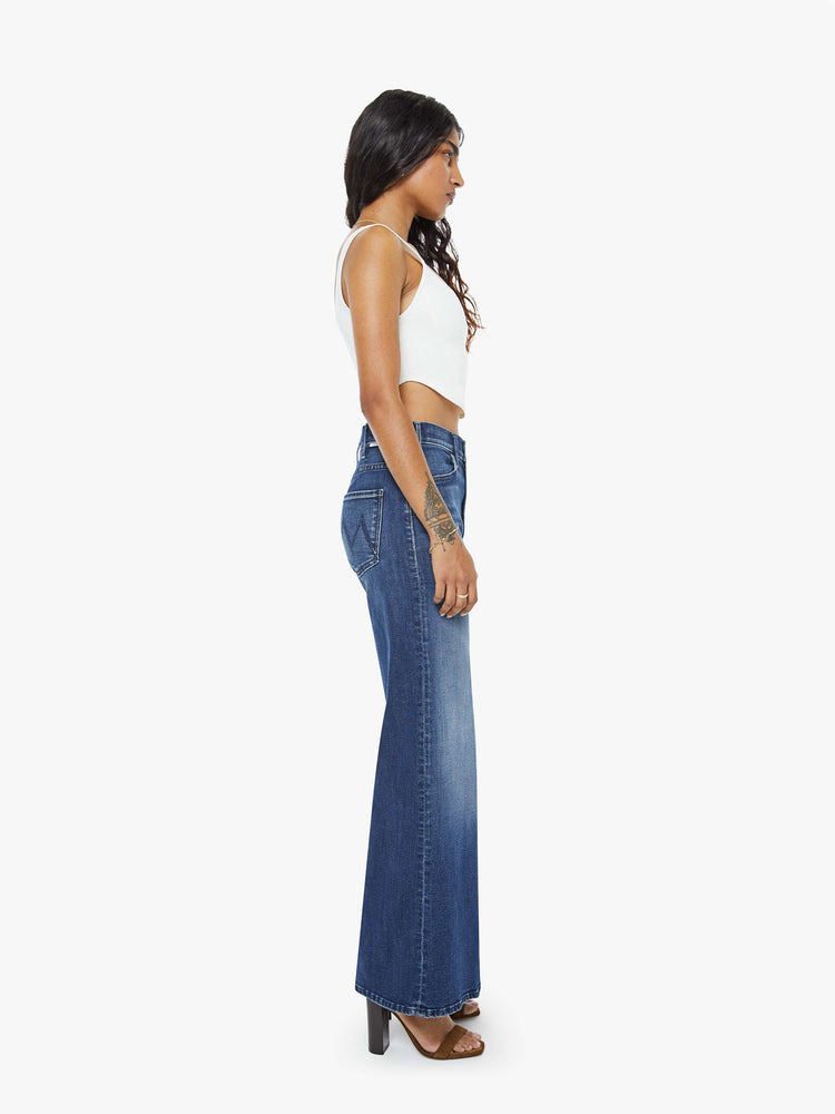 Side view of a petite woman in a dark blue  wide leg jeans have a high rise, zip fly, long 29-inch inseam and a clean hem.