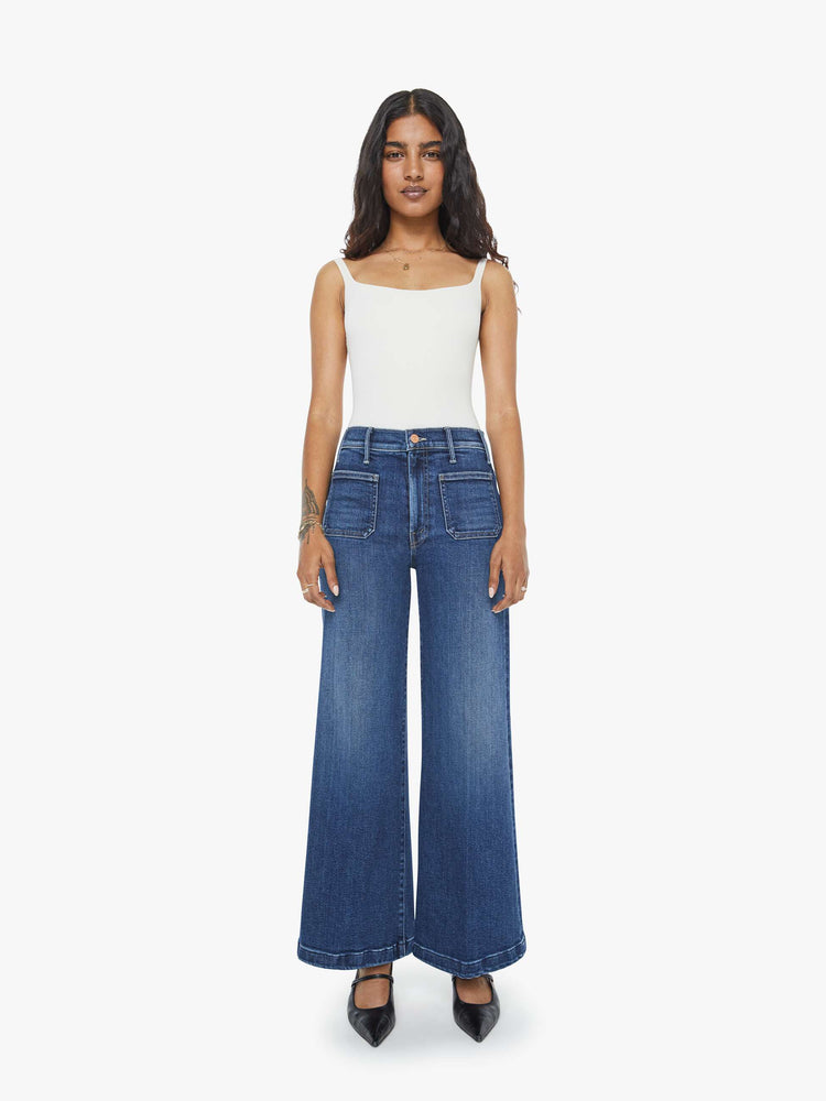 Front view of a petite woman in a  dark blue wide leg jeans with a high rise, zip fly, patch pockets, 28-inch inseam and a clean hem. 