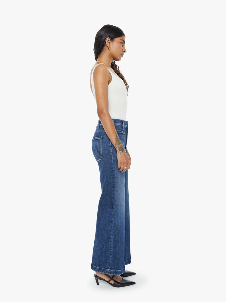 Side view of a petite woman in a  dark blue wide leg jeans with a high rise, zip fly, patch pockets, 28-inch inseam and a clean hem. 