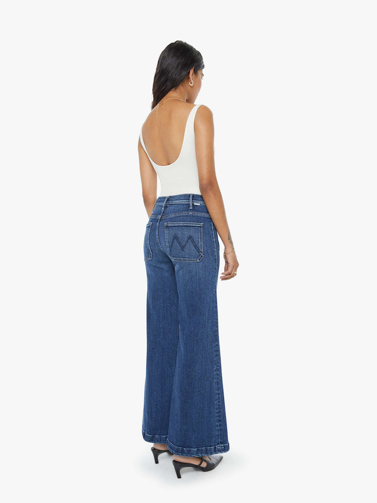 Back view of a petite woman in a  dark blue wide leg jeans with a high rise, zip fly, patch pockets, 28-inch inseam and a clean hem. 