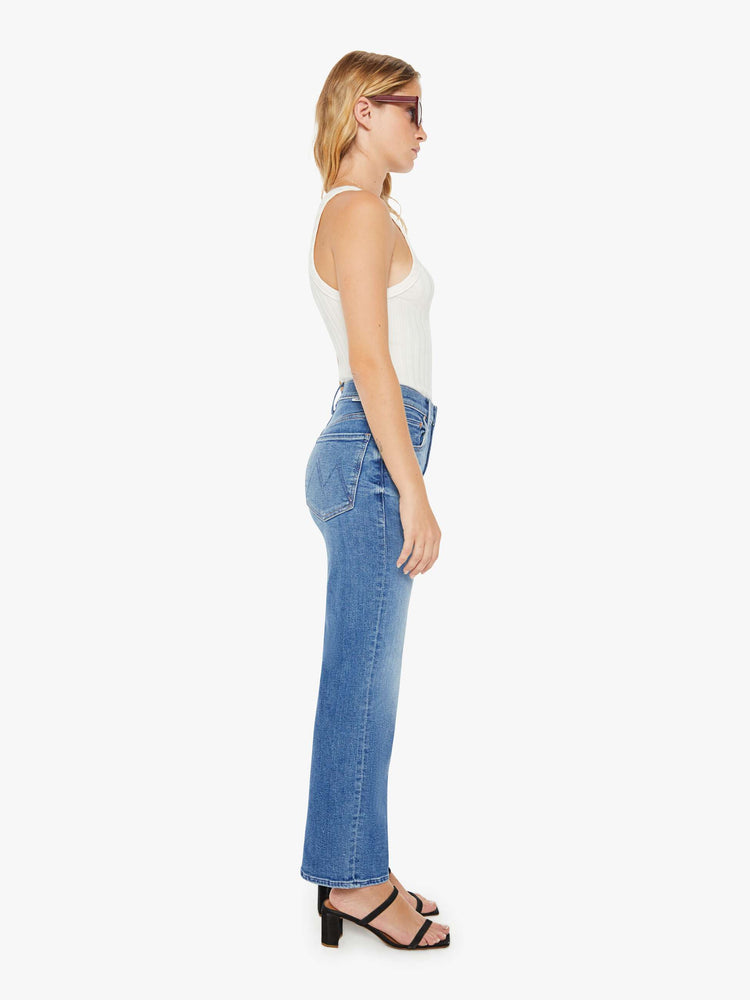 Side view of a petite woman high-waisted jeans with a wide straight leg, zip fly and clean ankle-length inseam in a mid blue wash.