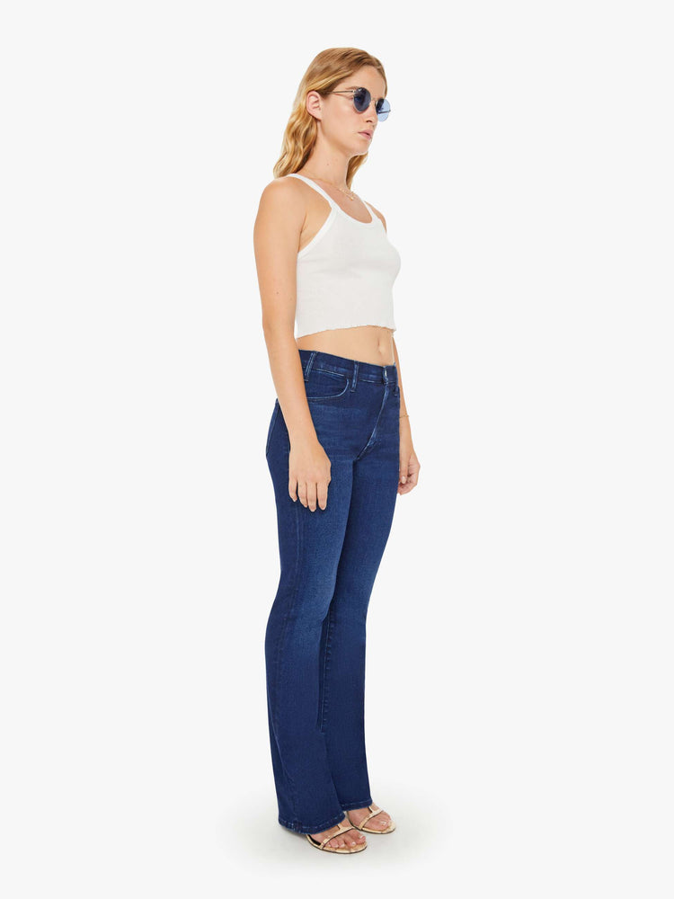Front view of a petite woman in a high-rise bootcut has a long inseam and a clean hem in a dark blue wash.