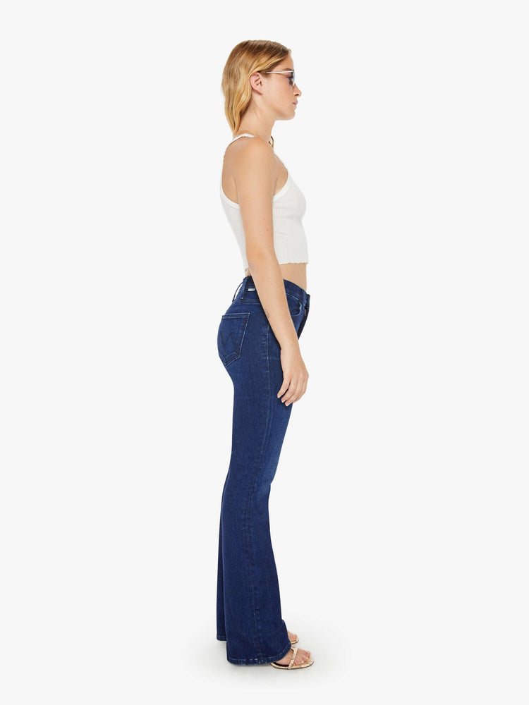 Side view of a petite woman in a high-rise bootcut has a long inseam and a clean hem in a dark blue wash.