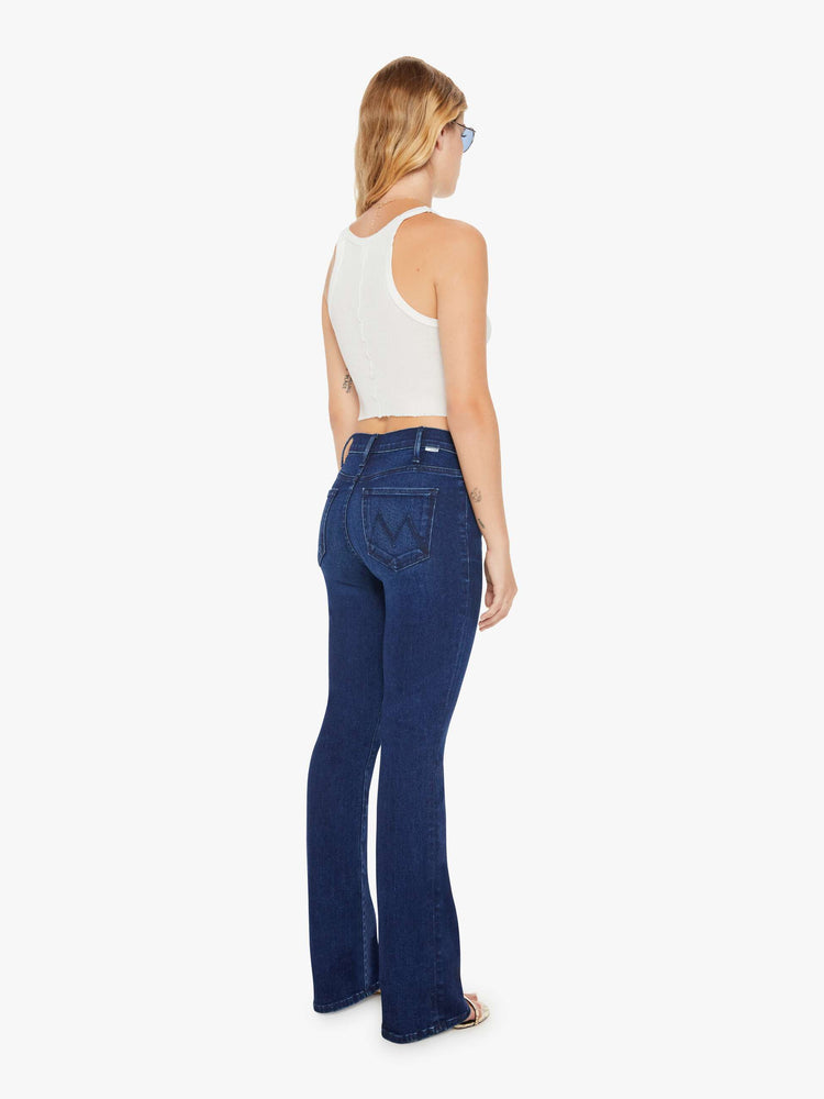 Back view of a petite woman in a high-rise bootcut has a long inseam and a clean hem in a dark blue wash.