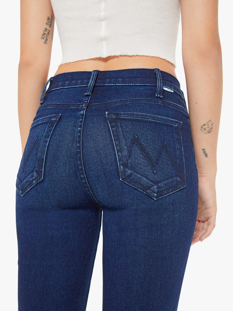 Close up view of a petite woman in a high-rise bootcut has a long inseam and a clean hem in a dark blue wash.