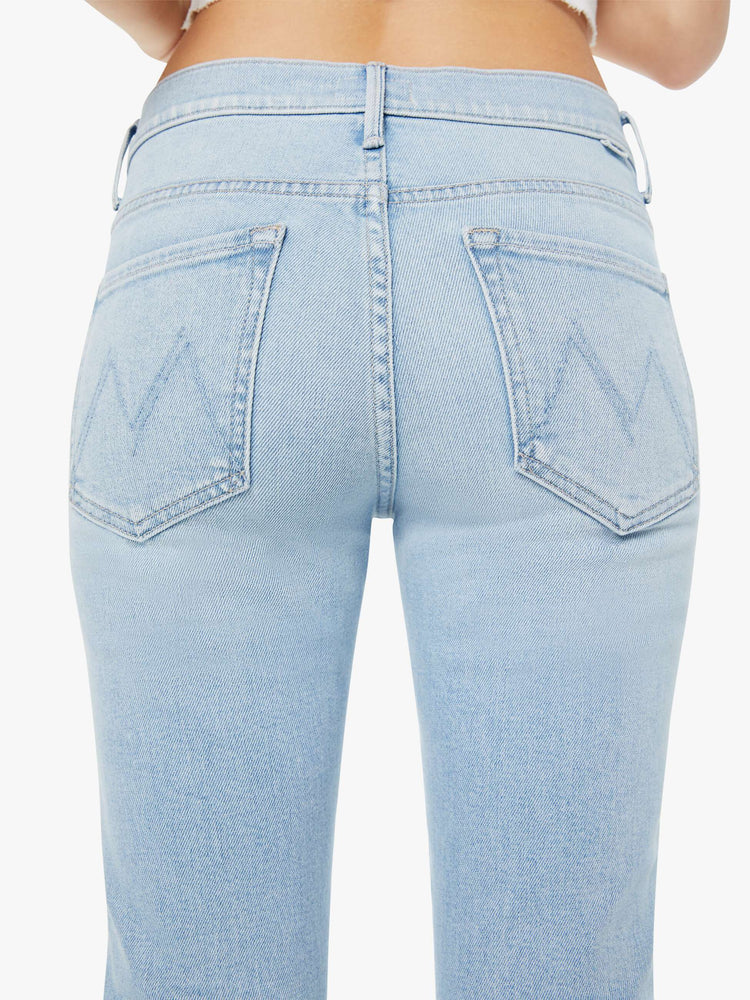 Detailed back view of a woman in light-blue high waisted bootcut jeans that have a clean hem with subtle whiskering and fading throughout.
