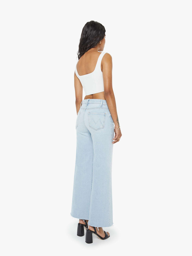 Back view of a petite woman in a light blue  wide leg pants with a zip fly, high rise, 29-inch inseam and a frayed hem. 