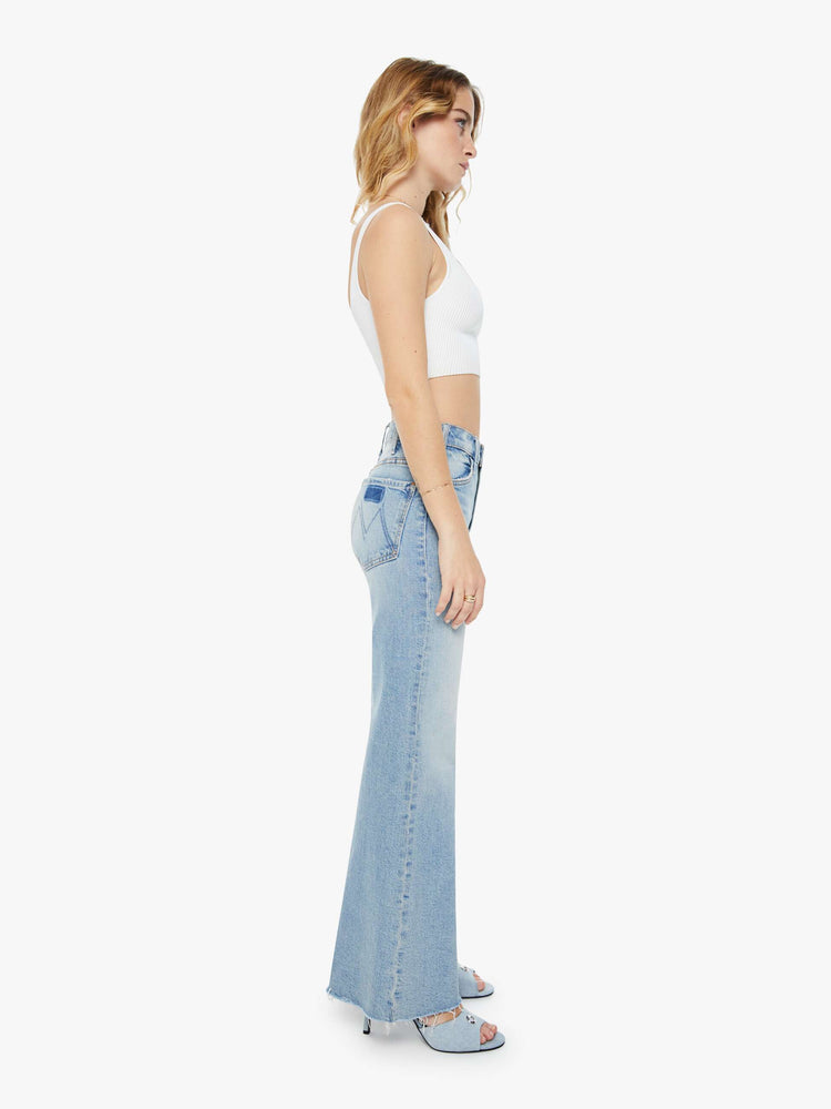 Side view of a woman in light blue 70s-inspired high waisted wide leg jeans that have a frayed hem with whiskering, fading and distressed details.