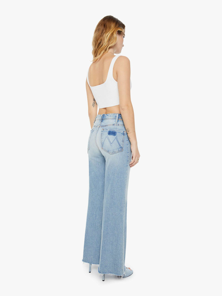 Back view of a woman in light blue 70s-inspired high waisted wide leg jeans that have a frayed hem with whiskering, fading and distressed details.