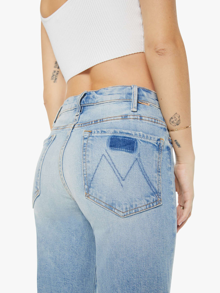 Detailed back view of a woman in light blue 70s-inspired high waisted wide leg jeans that have a frayed hem with whiskering, fading and distressed details.