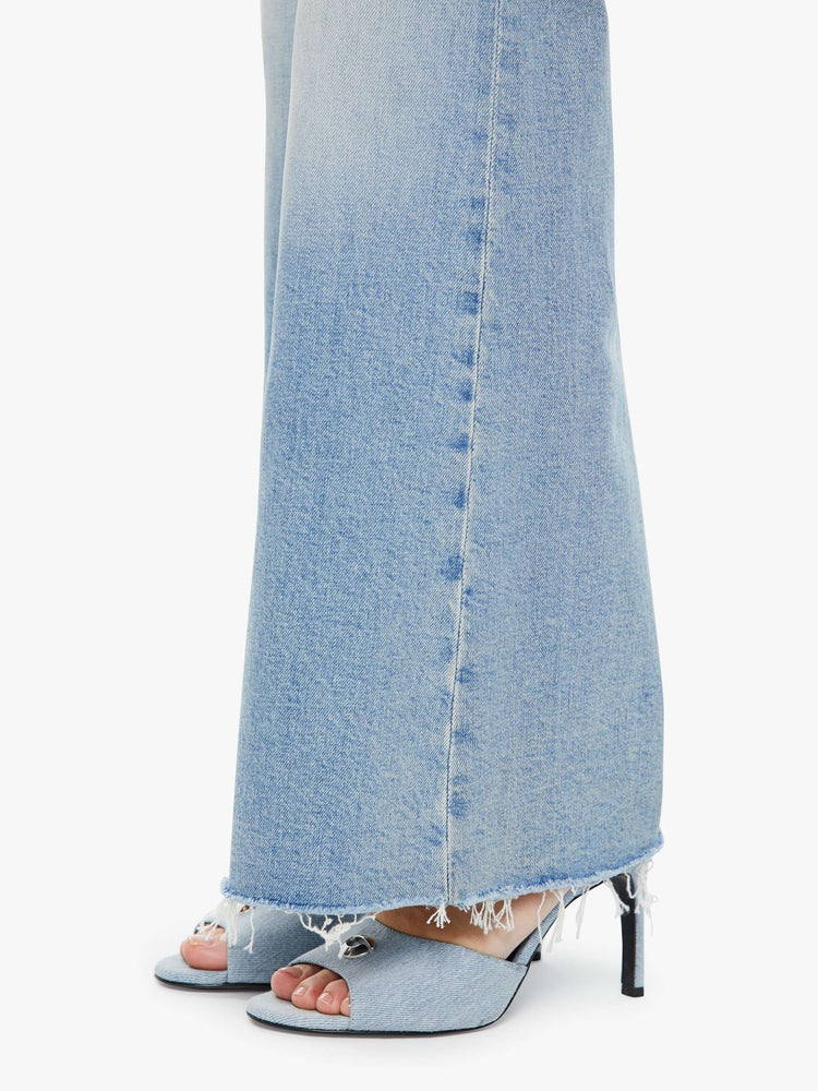 Detailed hem view of a woman in light blue 70s-inspired high waisted wide leg jeans that have a frayed hem with whiskering, fading and distressed details.