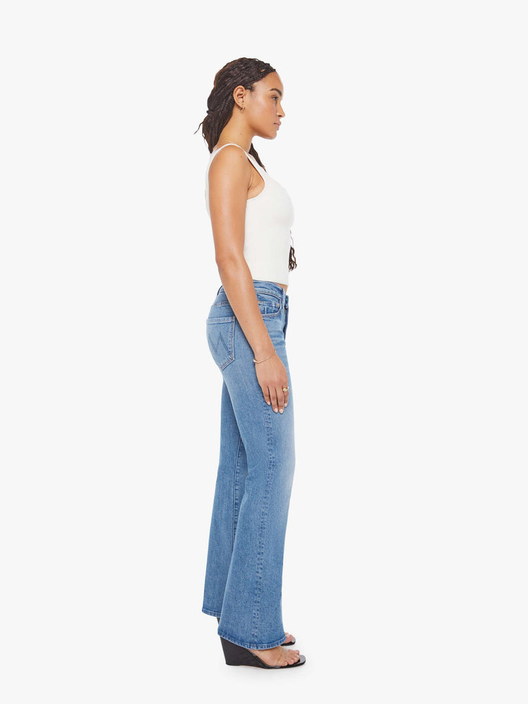 Side view of a petite woman in a mid blue bootcut jeans with a mid rise, zip fly and a long 29-inch inseam with a clean hem. 