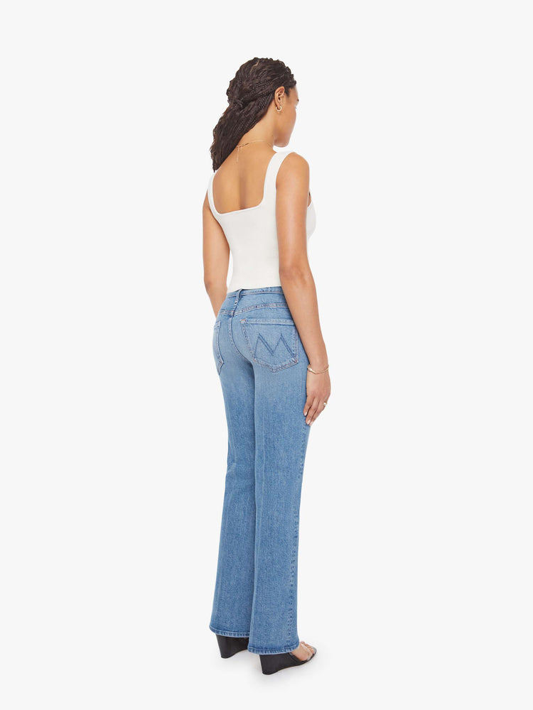 Back view of a petite woman in a mid blue bootcut jeans with a mid rise, zip fly and a long 29-inch inseam with a clean hem. 