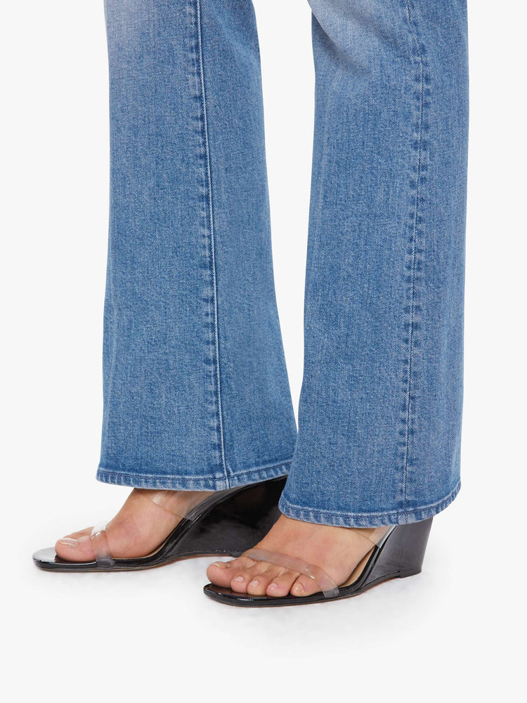 Hem view of a petite woman in a mid blue bootcut jeans with a mid rise, zip fly and a long 29-inch inseam with a clean hem. 