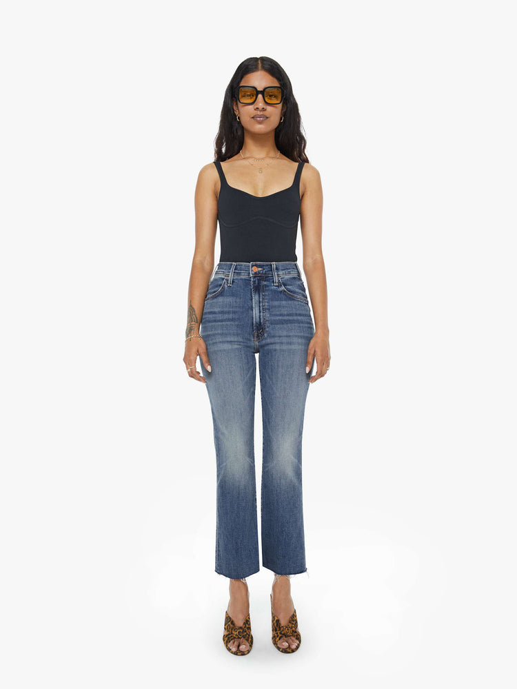 Full body view of a petite woman mid blue wash jean with a high-rise flare has an ankle-length inseam and a raw hem.