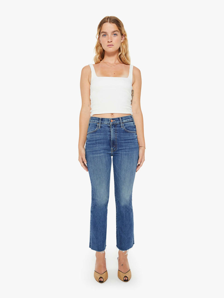 Full body view of a petite woman mid blue wash jean with a high-rise flare has an ankle-length inseam and a raw hem.