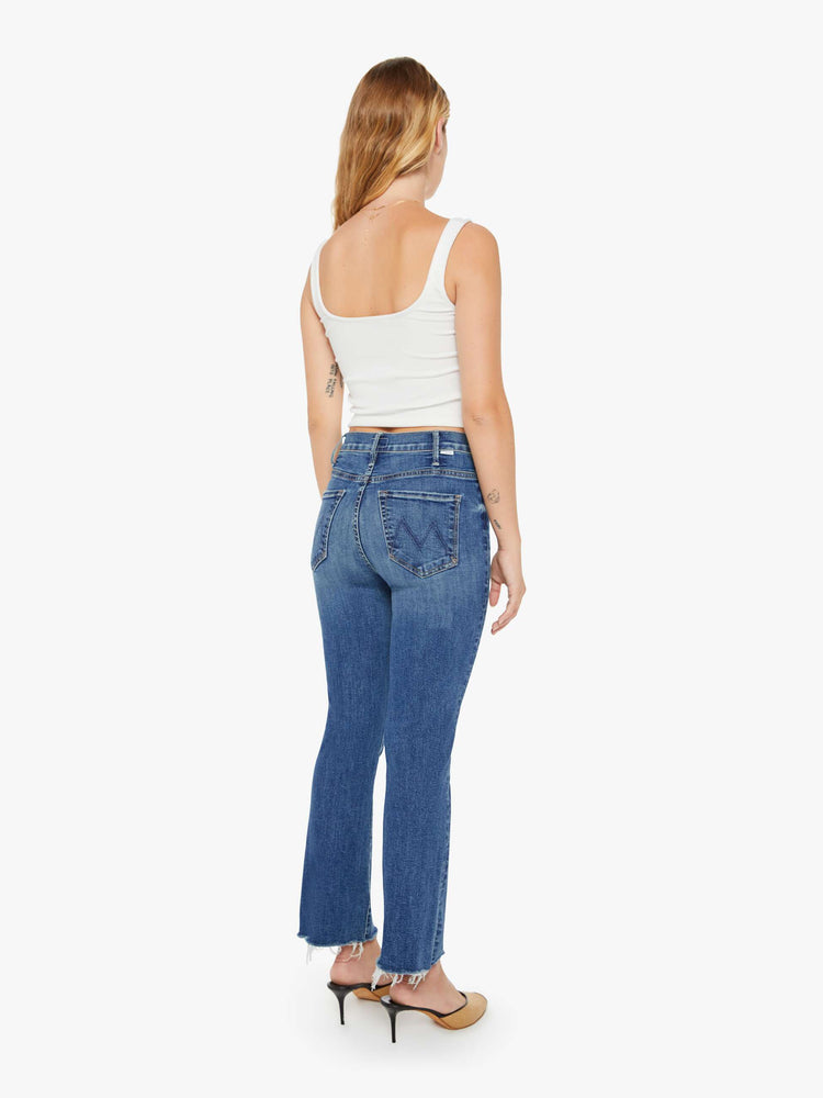 Back view of a petite woman mid blue wash jean with a high-rise flare has an ankle-length inseam and a raw hem.