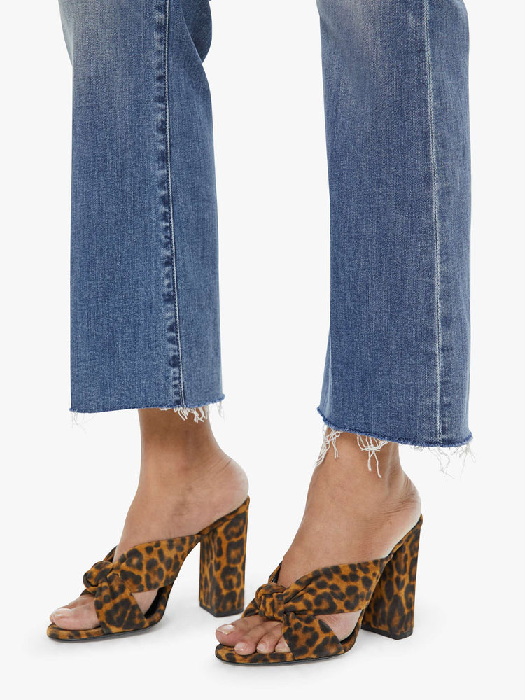 Hem  view of a petite woman mid blue wash jean with a high-rise flare has an ankle-length inseam and a raw hem.