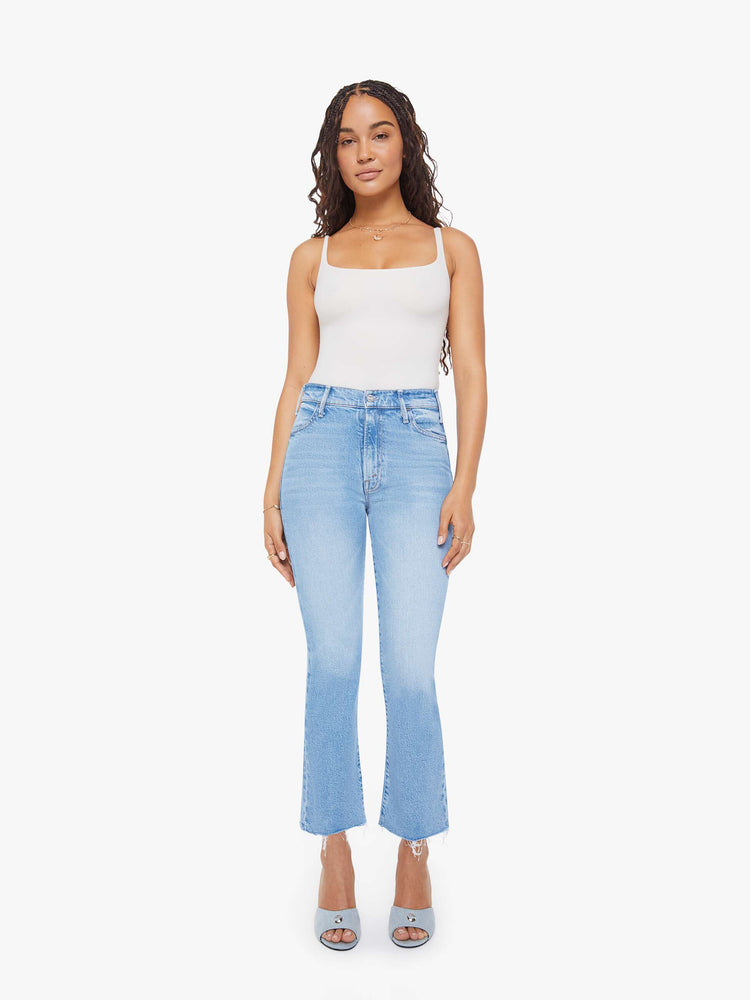 Front view of a woman in a light blue high-rise flare has an ankle-length inseam, zip fly and a frayed hem.