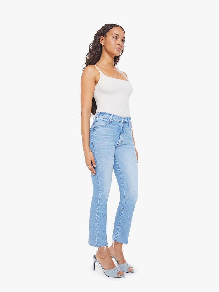 Side angle view of a woman in a light blue high-rise flare has an ankle-length inseam, zip fly and a frayed hem.