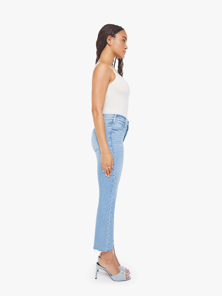 Side view of a woman in a light blue high-rise flare has an ankle-length inseam, zip fly and a frayed hem.