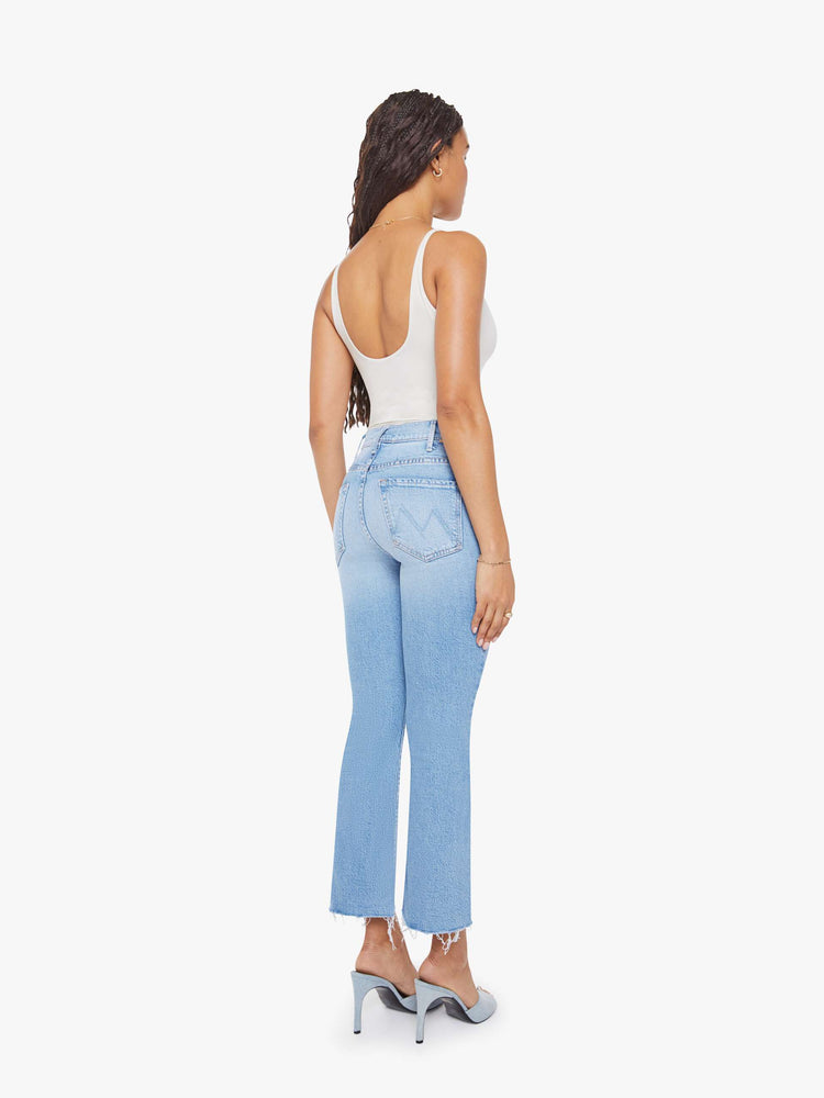 Back view of a woman in a light blue high-rise flare has an ankle-length inseam, zip fly and a frayed hem.