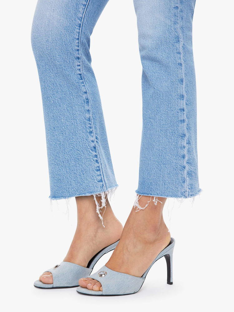 Hem close up view of a woman in a light blue high-rise flare has an ankle-length inseam, zip fly and a frayed hem.