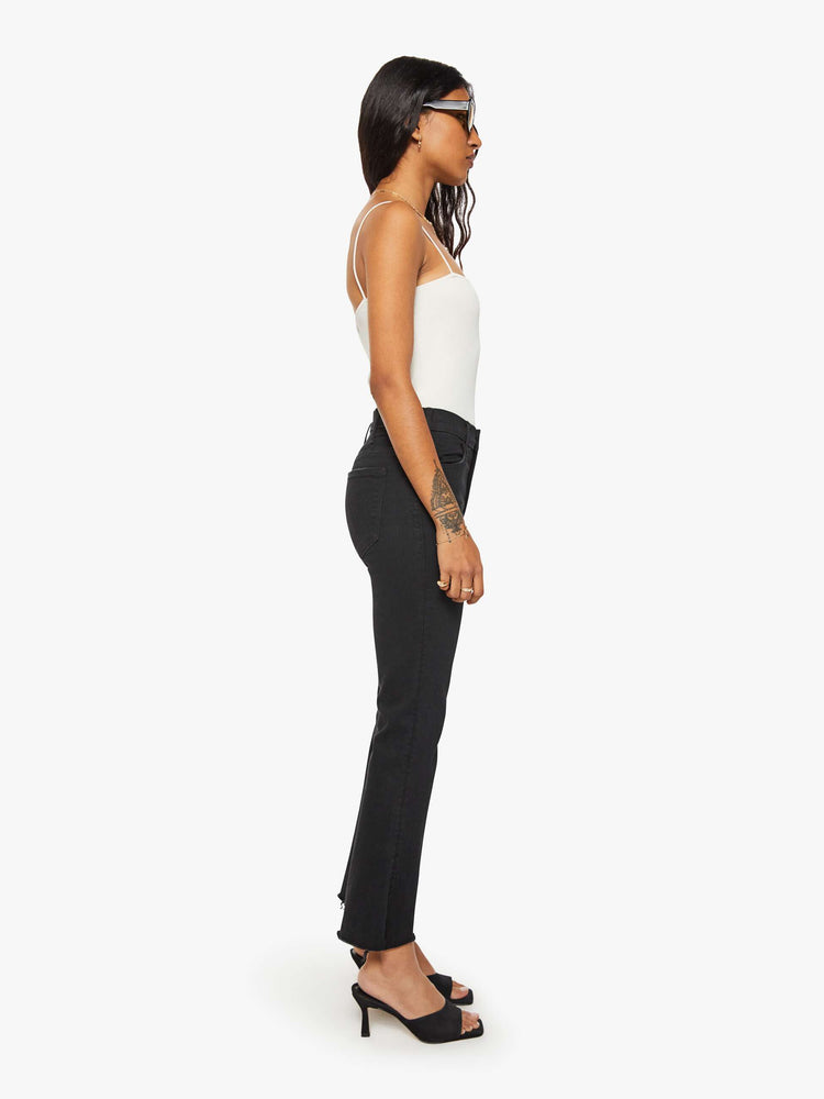 Side view of a woman black denim high-rise flare has an ankle-length inseam and a frayed hem.