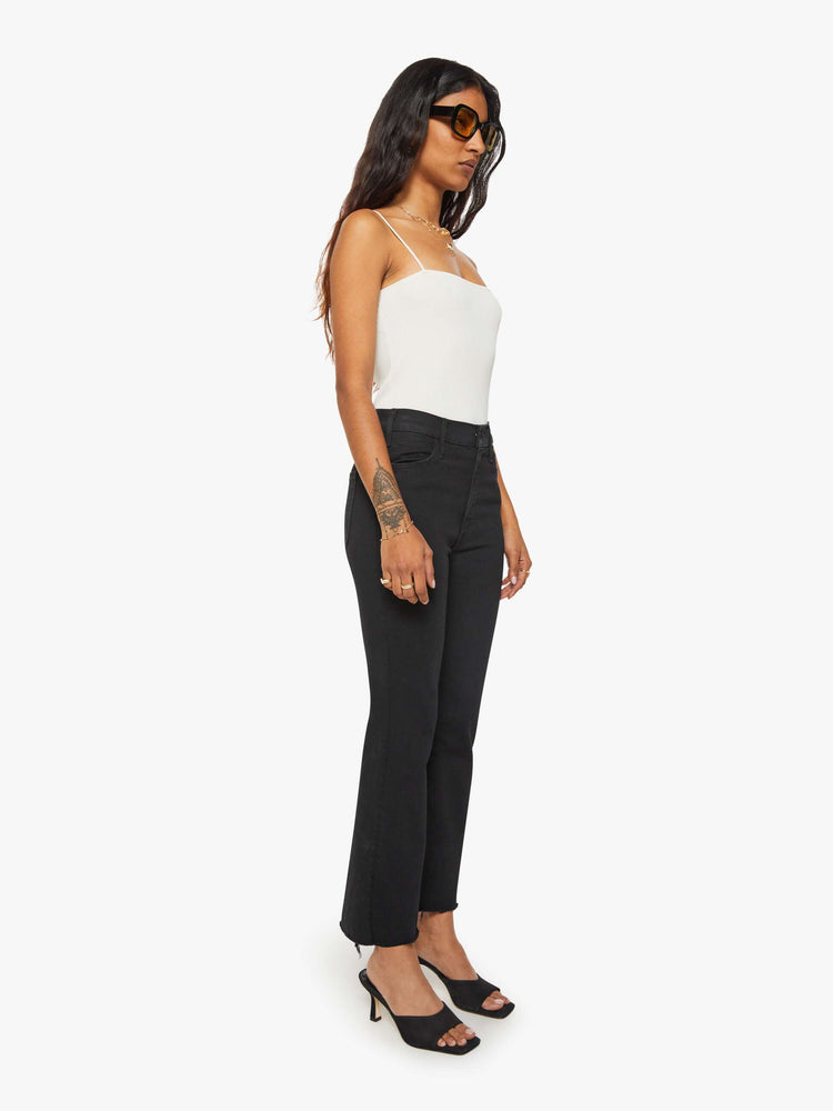 Side angle view of a woman black denim high-rise flare has an ankle-length inseam and a frayed hem.
