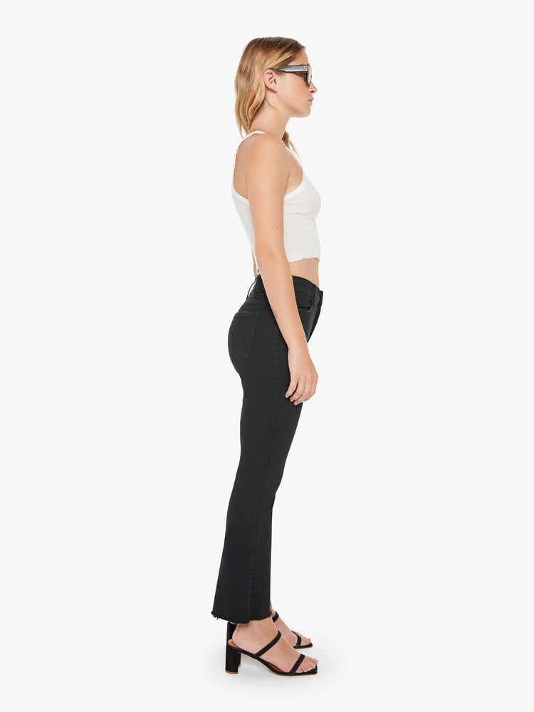 Side view of a woman black denim high-rise flare has an ankle-length inseam and a frayed hem.
