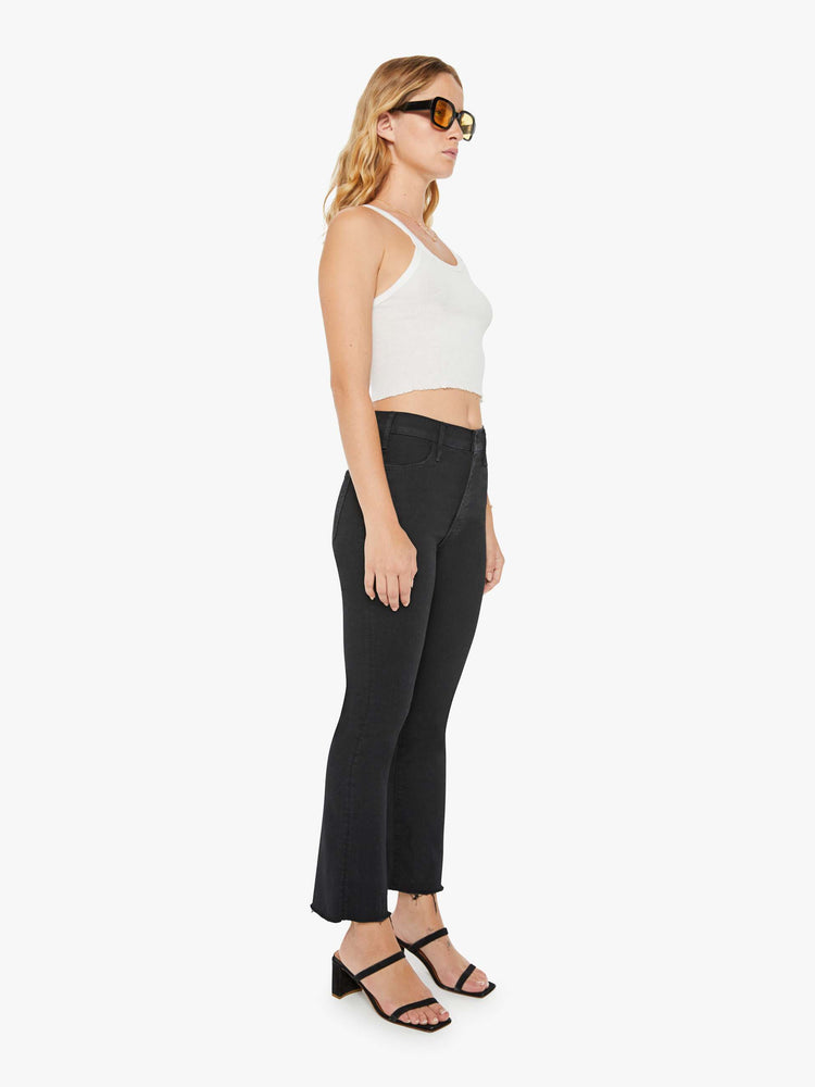 Side angle view of a woman black denim high-rise flare has an ankle-length inseam and a frayed hem.