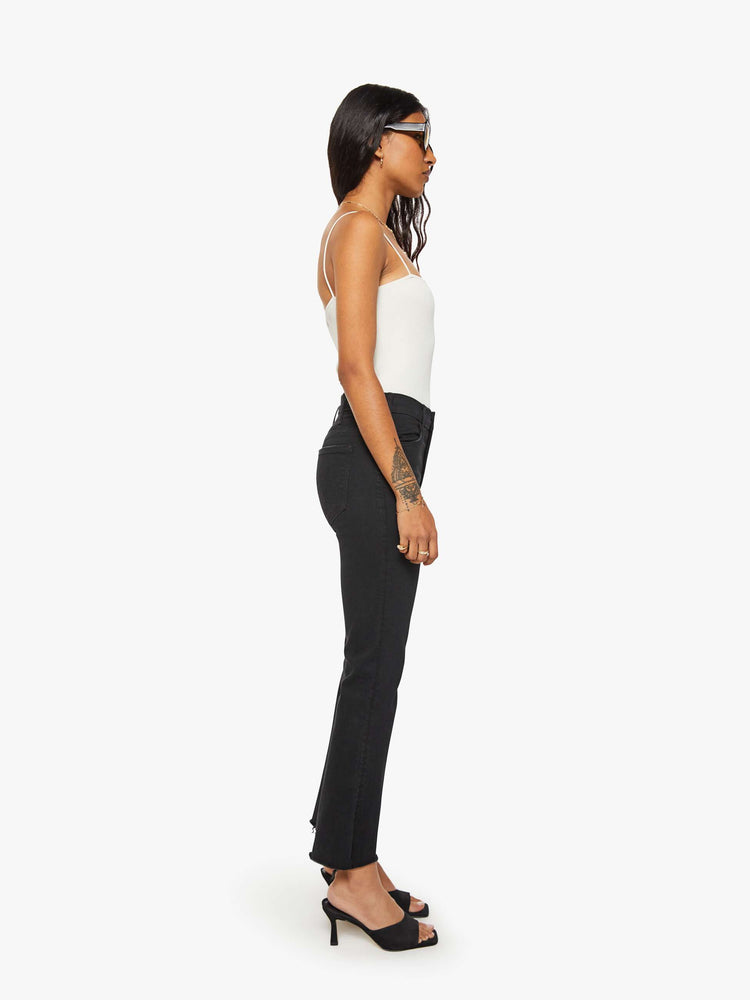 Side view of a woman black denim high-rise flare has an ankle-length inseam and a frayed hem.