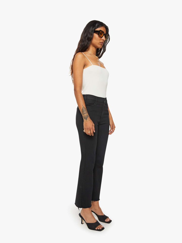 Side angle view of a woman black denim high-rise flare has an ankle-length inseam and a frayed hem.