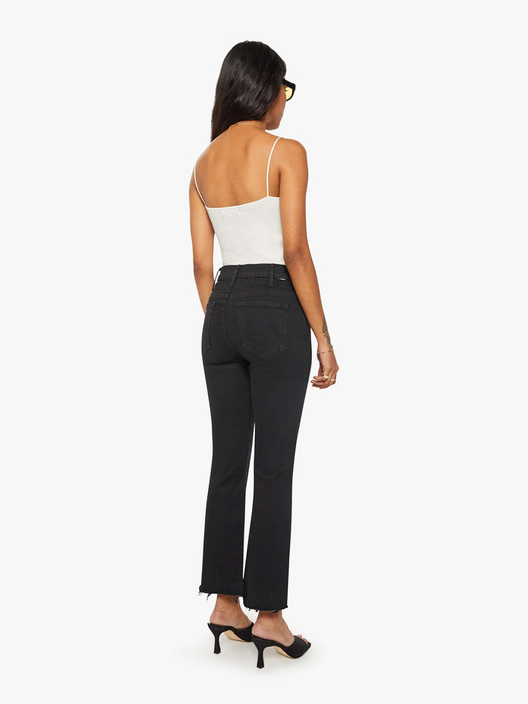 Back view of a woman black denim high-rise flare has an ankle-length inseam and a frayed hem.