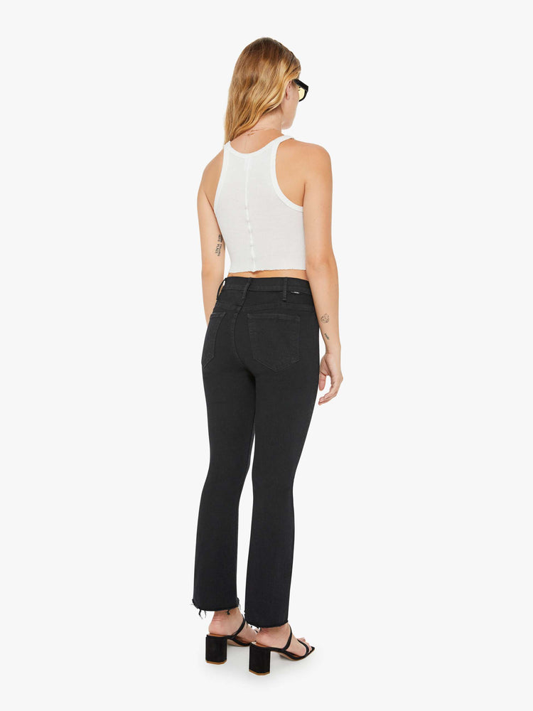 Back view of a woman black denim high-rise flare has an ankle-length inseam and a frayed hem.