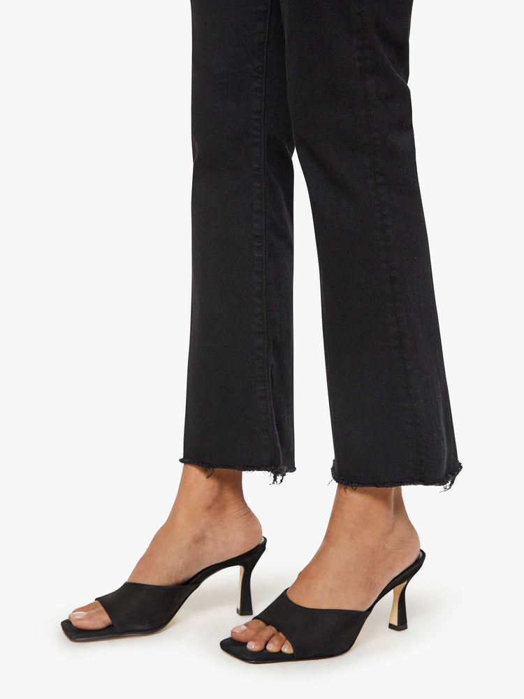 Hem close up of a woman black denim high-rise flare has an ankle-length inseam and a frayed hem.