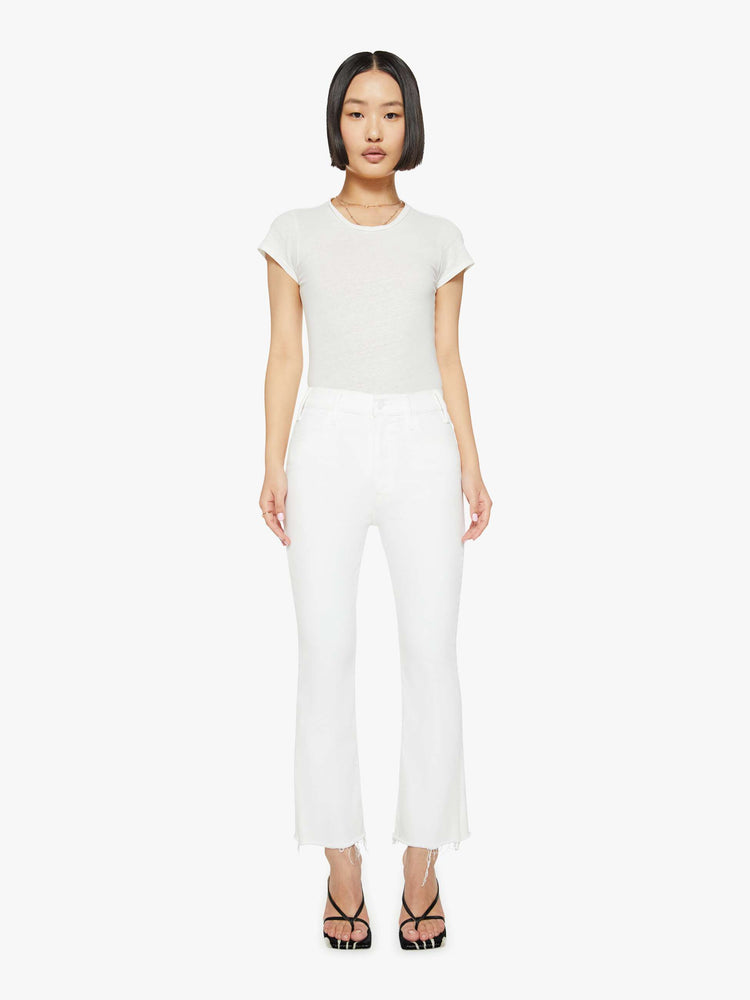 Front view of a woman in white high-rise flare jeans that have an ankle-length inseam and a raw hem.
