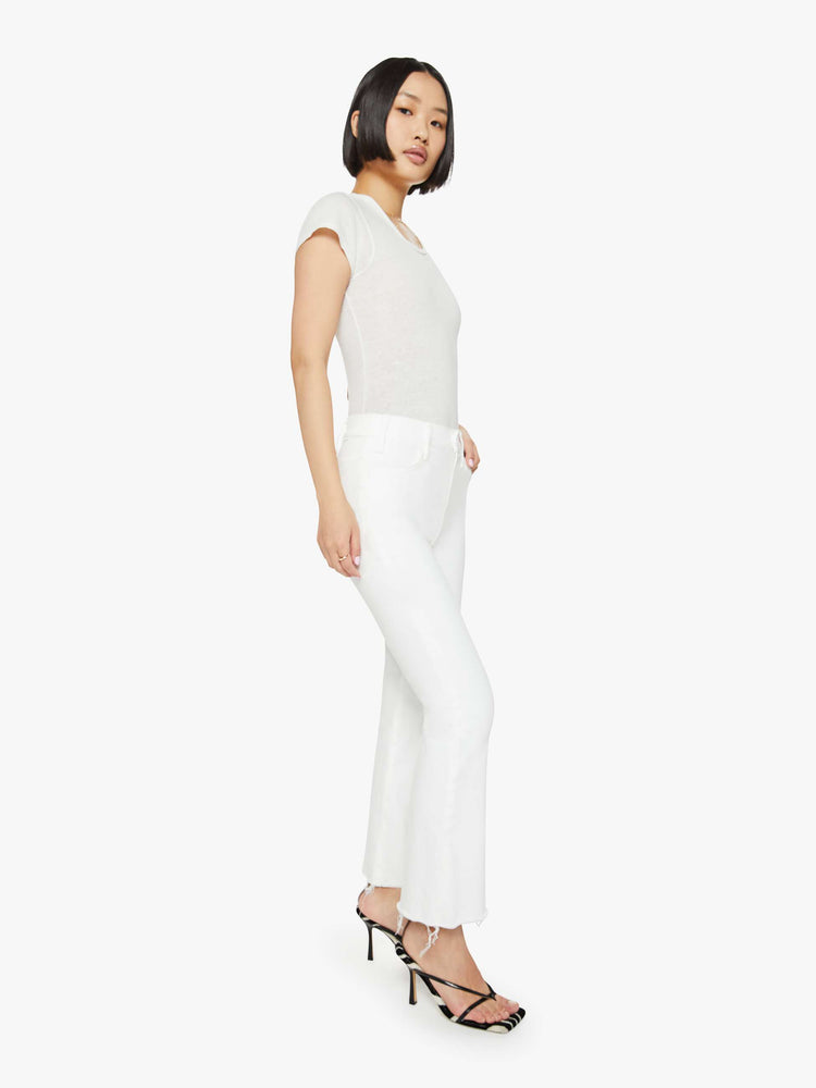 Angled front view of a woman in white  high-rise flare jeans that have an ankle-length inseam and a raw hem. 