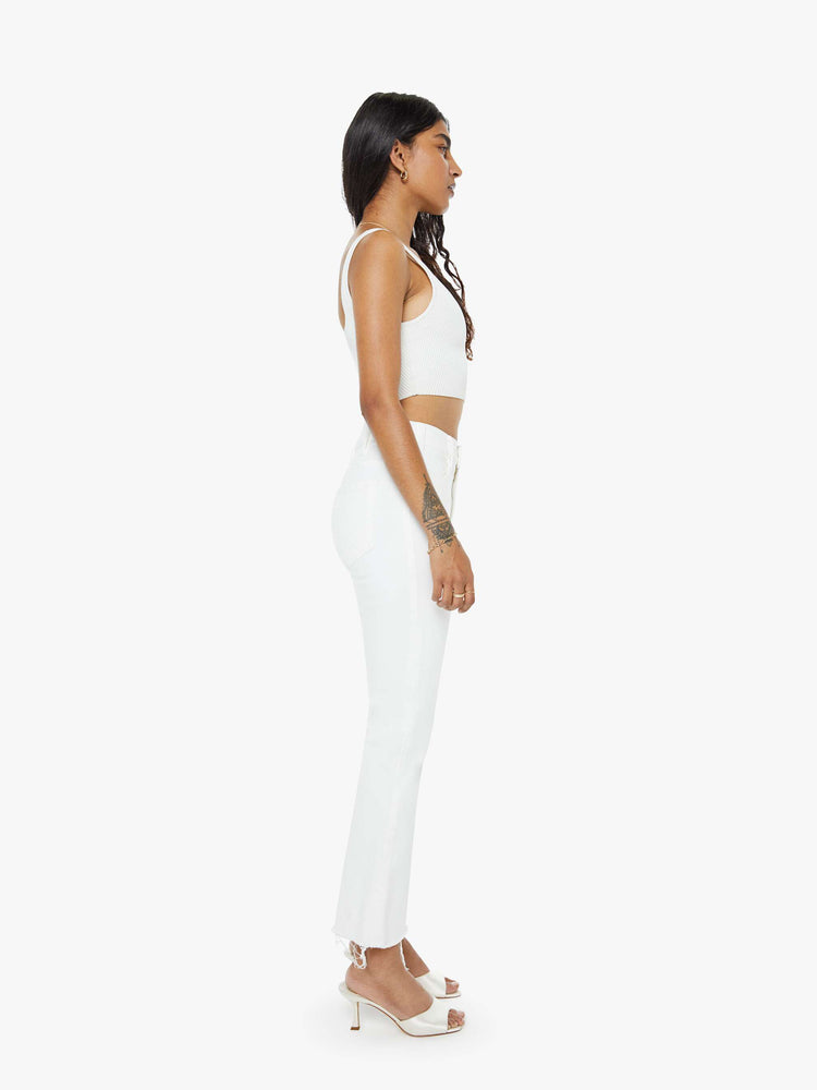 Side view of a woman in white high-rise flare jeans that have an ankle-length inseam and a raw hem.